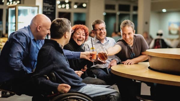 fröhliche Menschen in einer Bar, mindestens einer davon im Rollstuhl